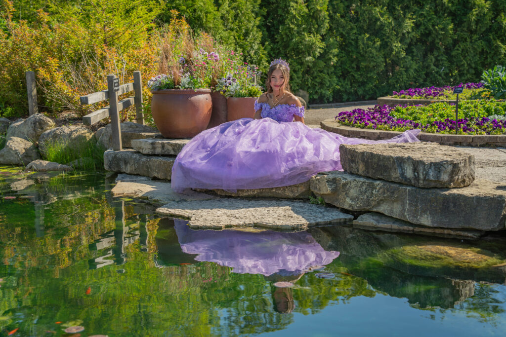 Quinceañera in a purple gown posing beside a garden pond with her reflection in the water during a Chicago quinceañera photoshoot.