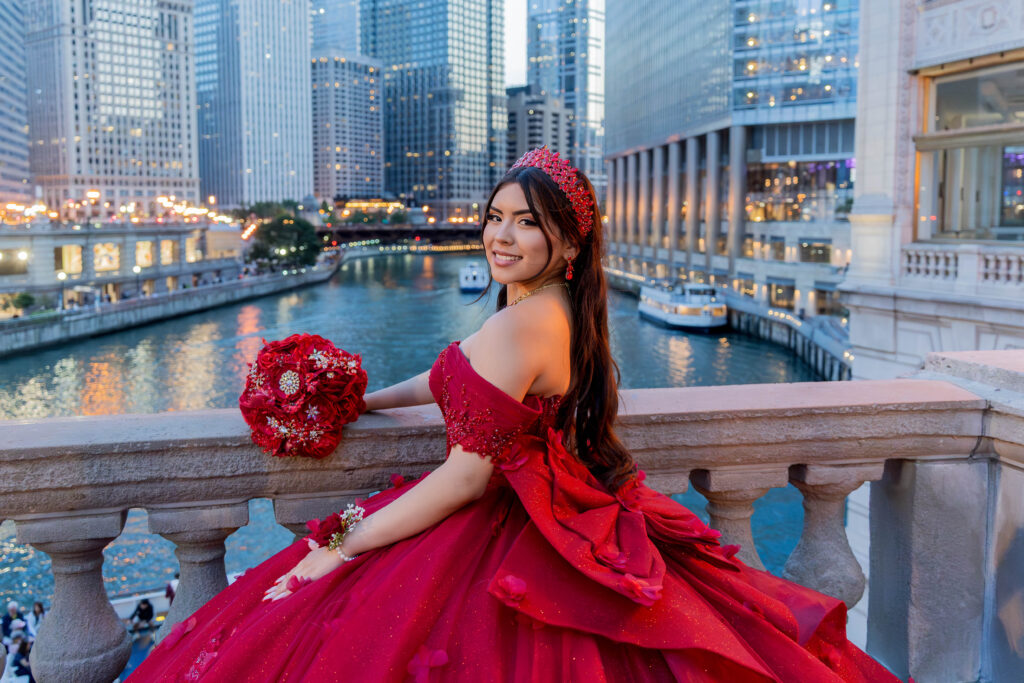 Quinceañera in a red dress posing along the Chicago Riverwalk with downtown Chicago architecture in the background.